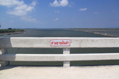 Sign board with text mounted on railing of bridge over sea