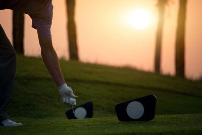 Low section of person playing with ball in grass during sunset