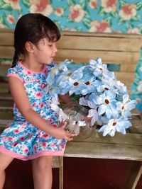 Girl holding artificial flowers in vase while sitting on bench