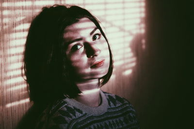 Close-up portrait of young woman standing against wall at home
