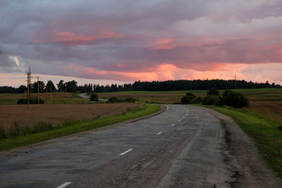 Road passing through field against cloudy sky