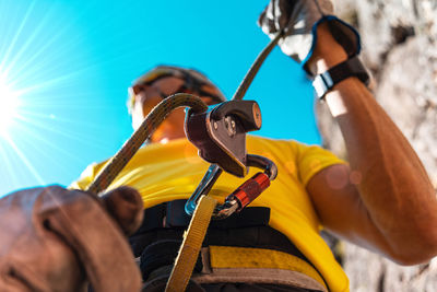 Low angle view of man holding safety harness against blue sky