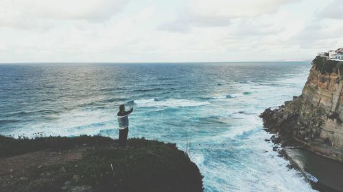 Man photographing sea while standing on cliff