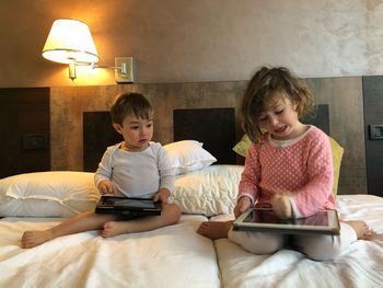 Siblings using digital tablet on bed at home