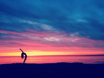 Silhouette woman doing yoga by sea against cloudy sky during sunset