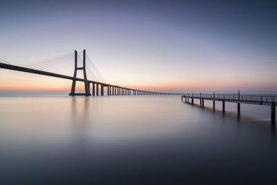 Suspension bridge over sea against sky during sunset