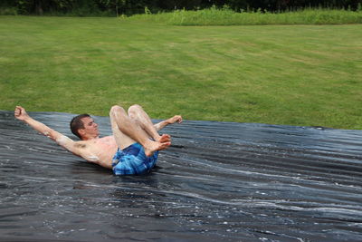Young man sliding on water slide over field