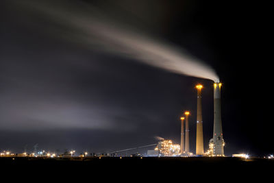 Low angle view of illuminated factory against sky at night