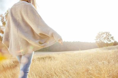 Rear view of woman walking on grassy field against clear sky during sunny day