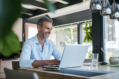 Smiling mature man at home using a laptop at table