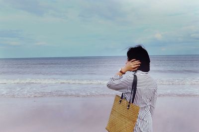 Rear view of woman standing at shore of beach against sky