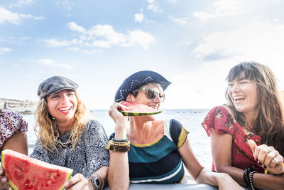 Smiling women eating watermelon against sky