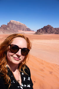 Portrait of woman wearing sunglasses in desert against sky