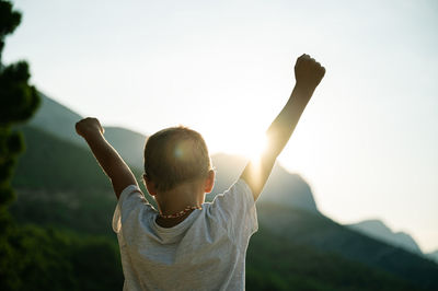 Rear view of woman with arms raised against sky