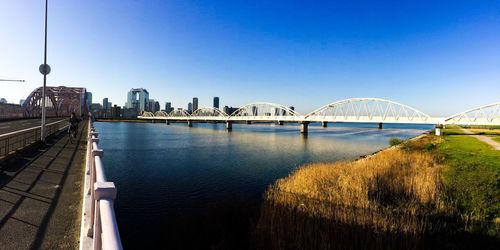 View of suspension bridge in front of sea against clear blue sky