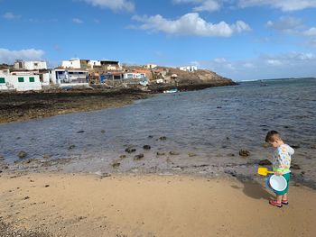 Side view of boy standing at beach against blue sky