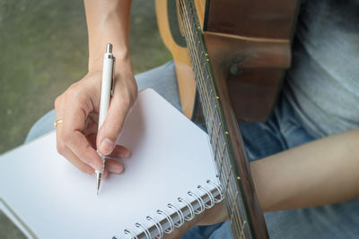 Midsection of woman with guitar writing on book