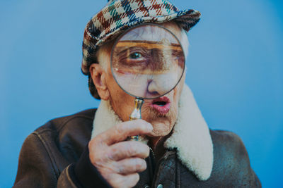 Portrait of senior woman looking through magnifying glass against blue background