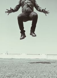 Low section of man jumping over field against clear sky