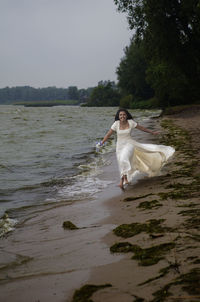 Woman with arms raised on shore against sky