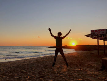 Man standing at beach against sky during sunset