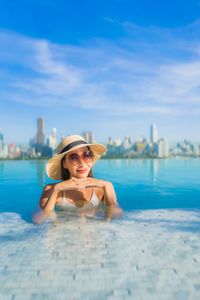 Portrait of young woman in swimming pool against sky