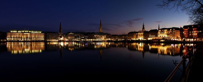Panoramic view of buildings glowing by alster river at night