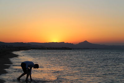 Silhouette woman standing by sea against orange sky