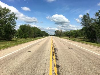 Surface level of road amidst trees against sky