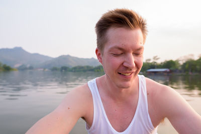 Portrait of smiling young man in lake against sky