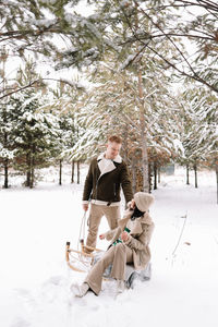 A man and woman in love have fun and ride a sleigh in the forest among the trees in winter in nature