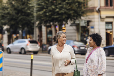 Smiling disabled woman talking with female friend while standing at street in city