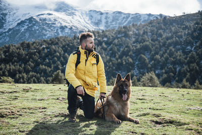 Young man with yellow jacket and backpack plays with german shepherd dog in the mountains.