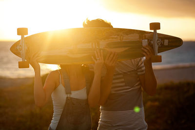 Couple with skateboard standing on field during sunset