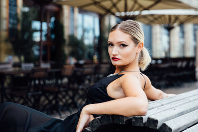 Portrait of confident young woman sitting on bench in city