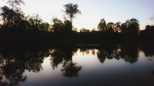 Reflection of silhouette trees in lake against sky