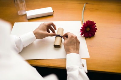 High angle view of woman holding white paper and flower on table