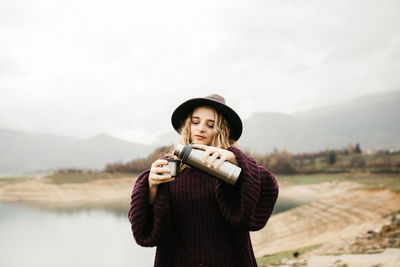 Portrait of young woman wearing hat standing against sky