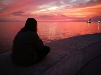 Silhouette woman sitting by sea against sky during sunset