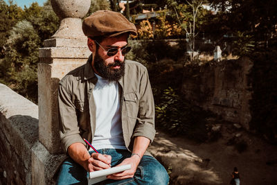 Man writing in book while sitting outdoors