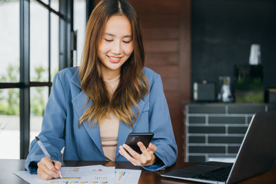 Portrait of young businesswoman using mobile phone while sitting at office