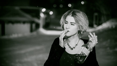 Close-up of young woman smoking cigarette while holding alcohol bottle at night