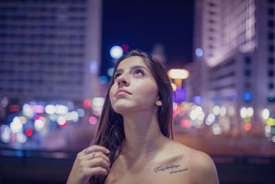 Young woman looking up at illuminated city