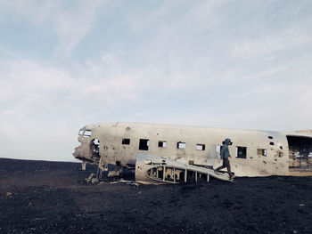 Side view of man walking by abandoned airplane against sky