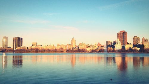 Buildings in manhattan against sky with reflection in jacqueline kennedy onassis reservoir at central park