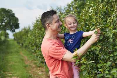 Smiling father with daughter touching plants at agricultural field