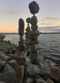 Stack of stones on beach against sky during sunset
