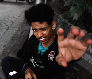 High angle portrait of young man gesturing while sitting on street