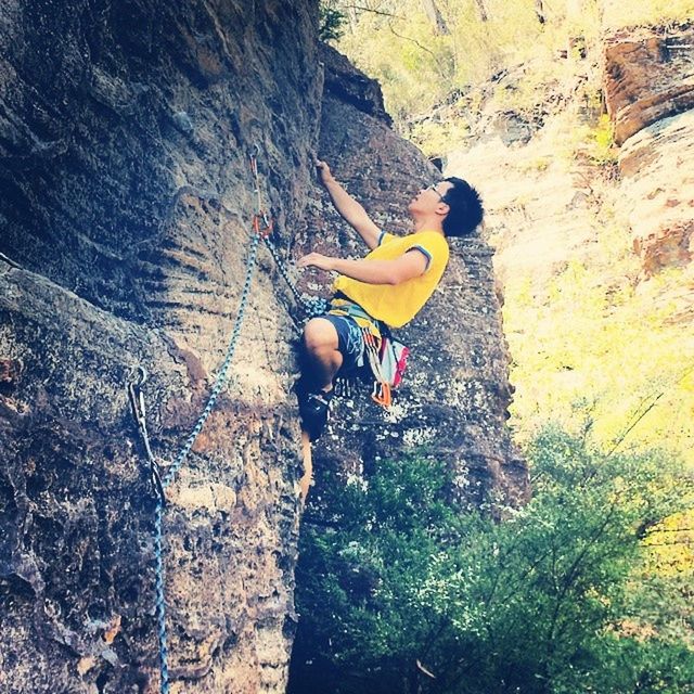 lifestyles, leisure activity, full length, men, adventure, rock - object, holding, tree, enjoyment, risk, casual clothing, nature, person, jumping, sunlight, day, outdoors