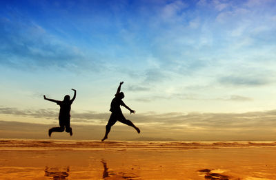 Silhouette people jumping over sea against sky during sunset